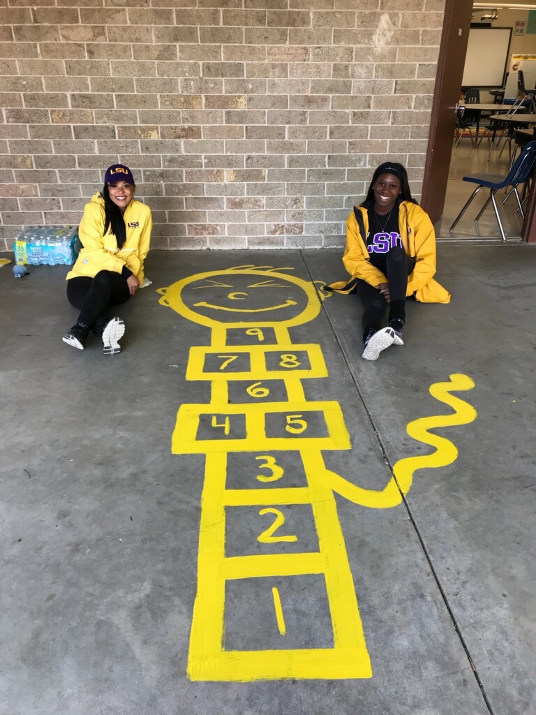 Alaysia and fellow black female student pose with a yellow hopscotch diagram at local elementary school.