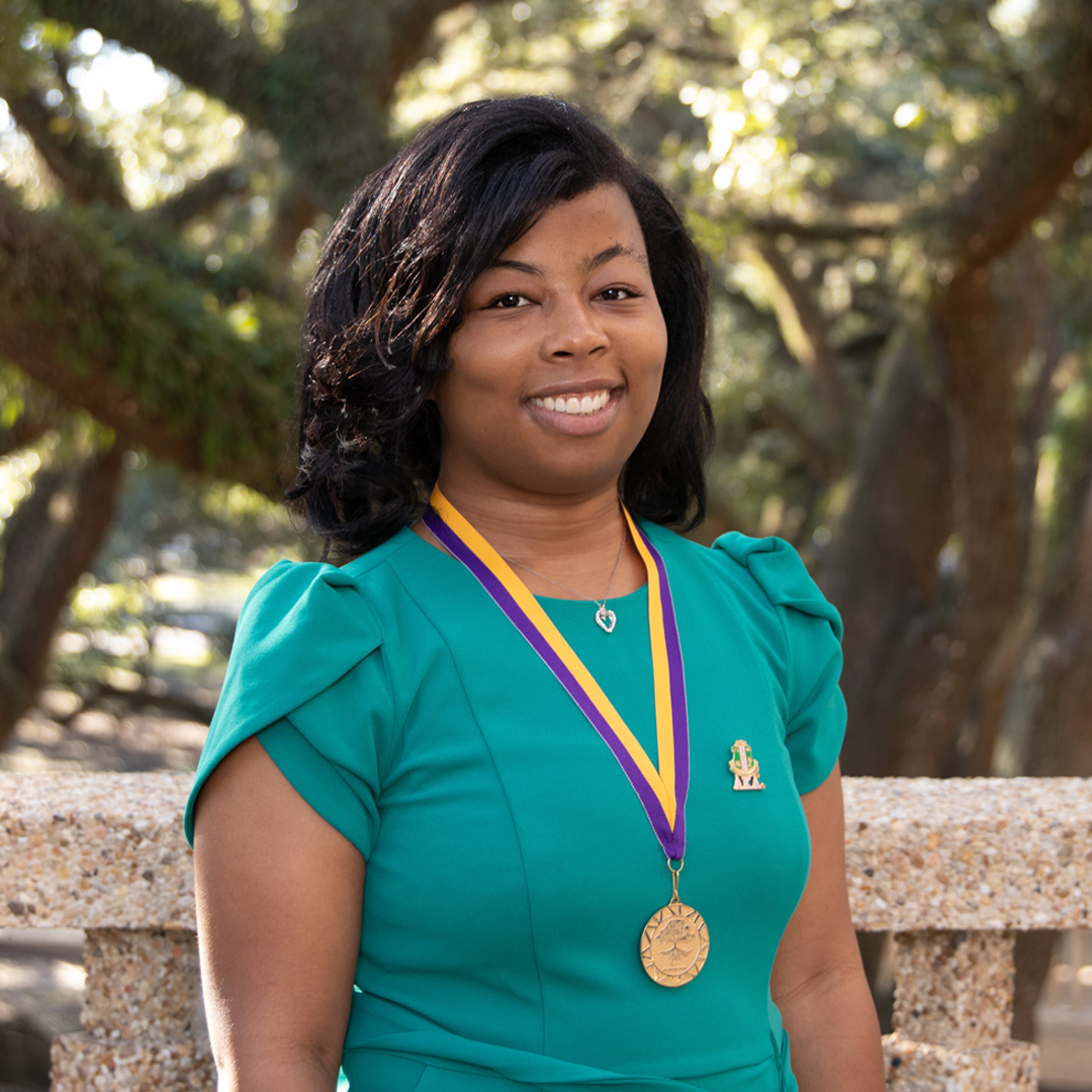 Student in green blouse smiles with purple and gold ribbon and medal around neck.