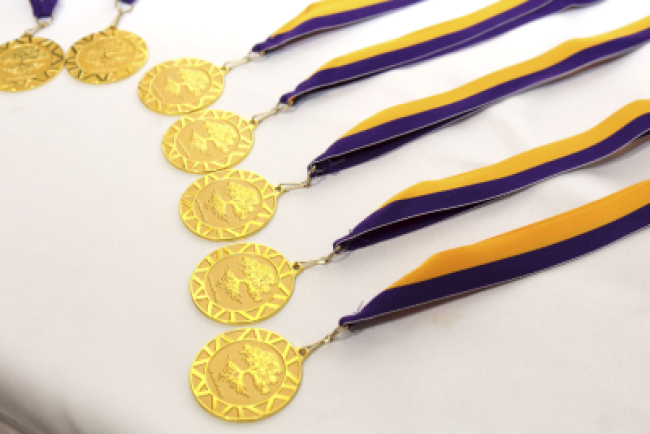 gold medals engraved with an oak tree, hanging from a purple and gold ribbons, rest on a white tablecloth.