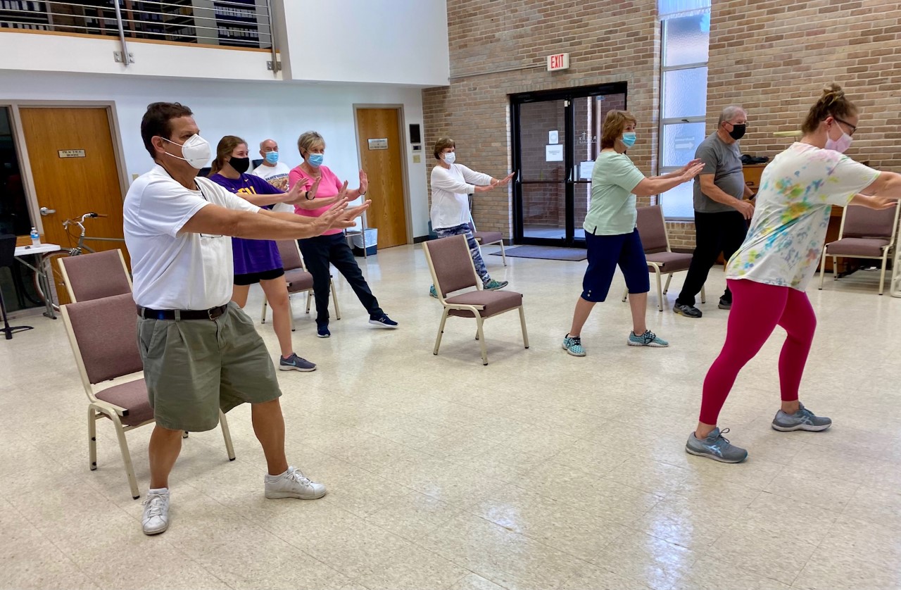 group of senior citizens practice tai chi together in building