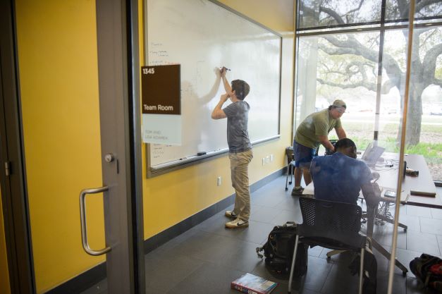 Three students work in a team room on a project