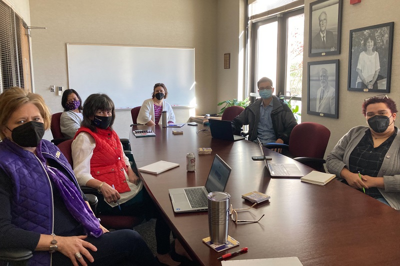 three people in COVID masks sit around a conference table