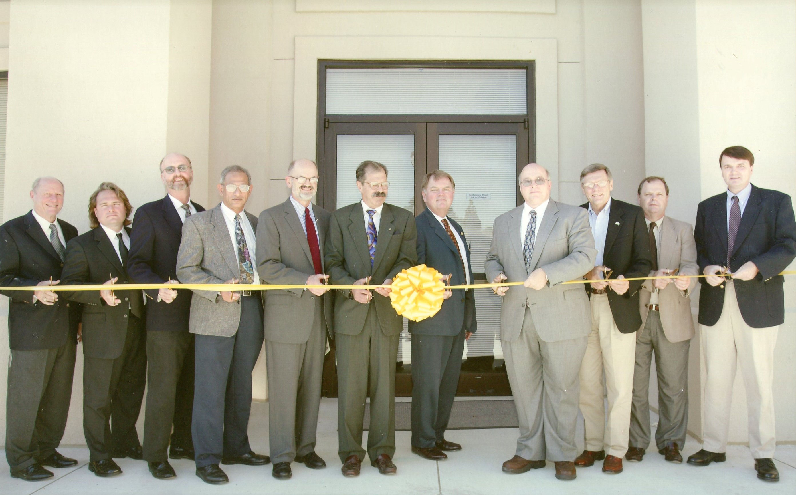 a group of people poised to cut a large yellow ribbon in front of a building