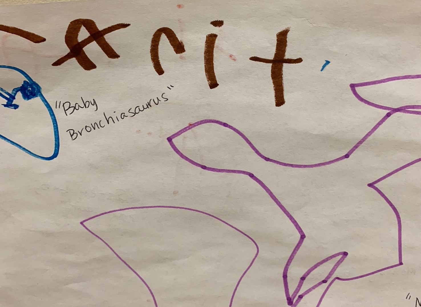 Child's writing sample in brown marker and depiction of a dinosaur