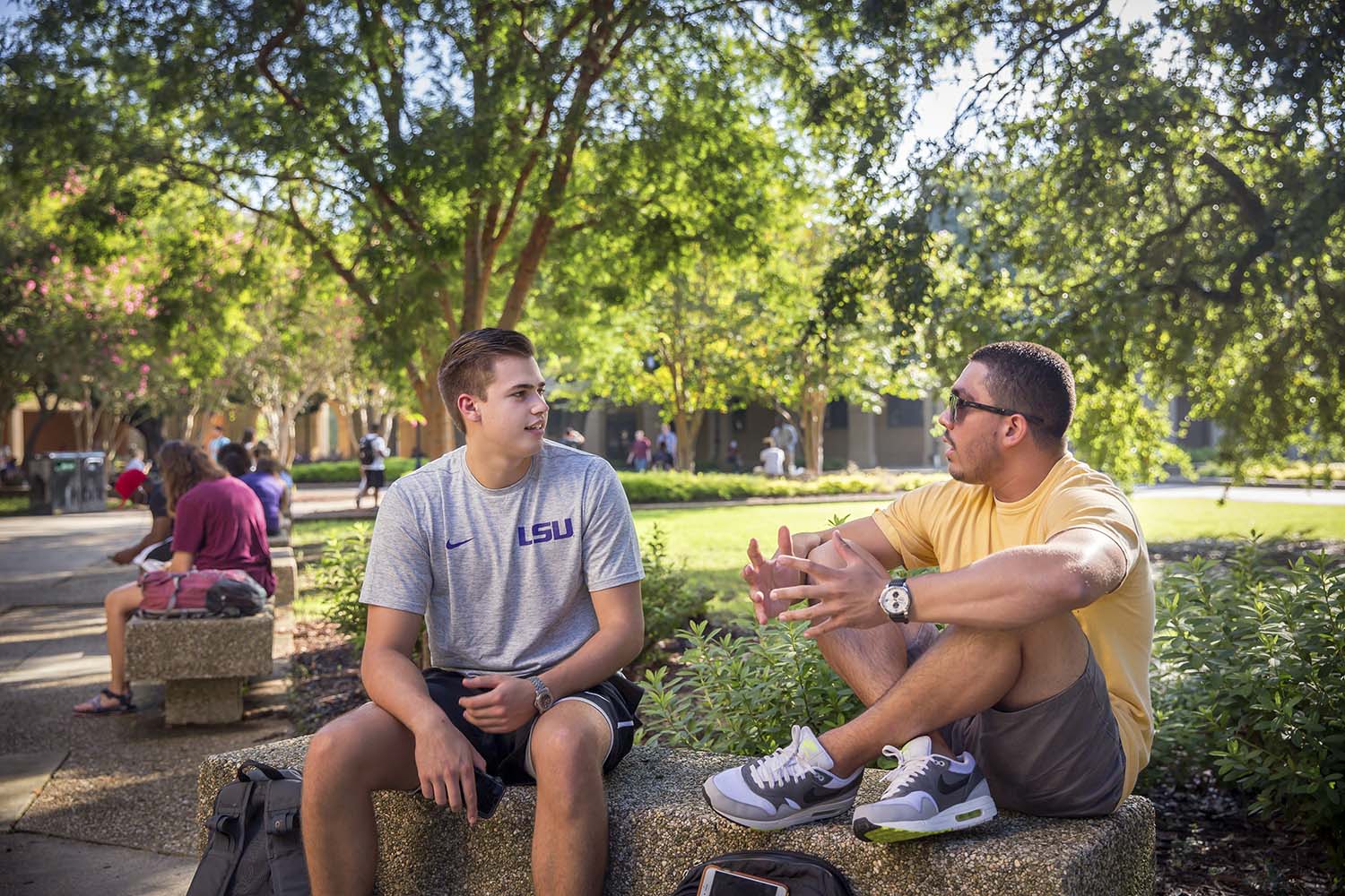 two male LSU students sitting on bench and talking in the quad
