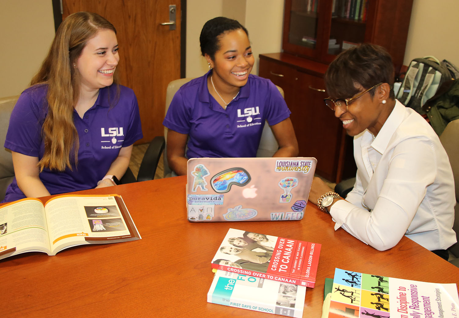 LSU teacher candidates sitting at conference table with professor with books and laptop.