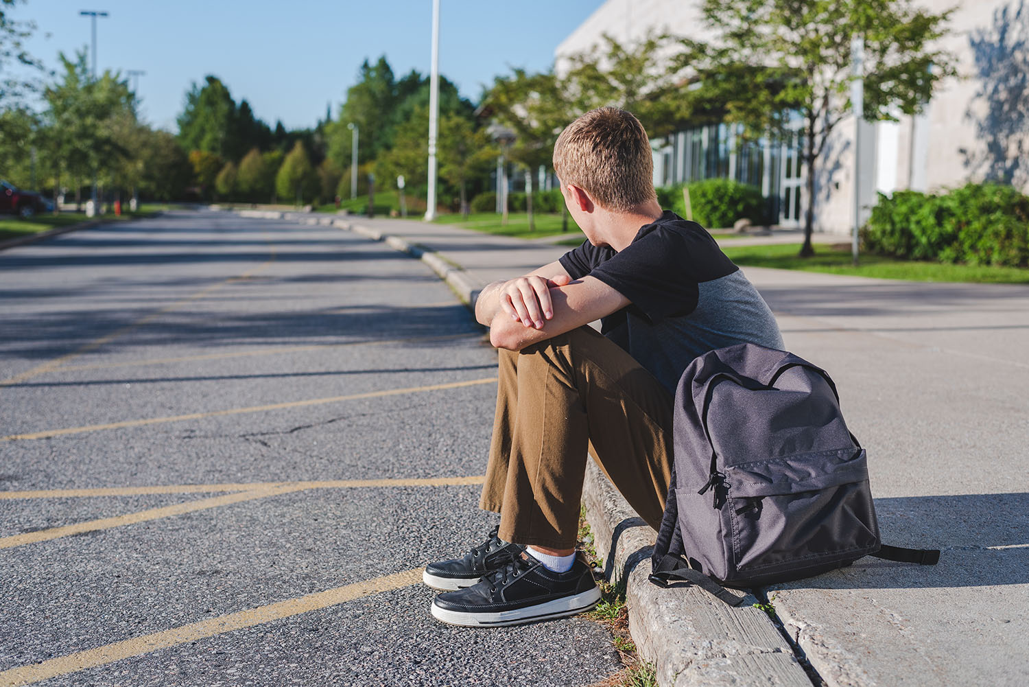boy sitting on a curb next to an empty school