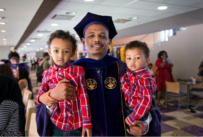 PhD student in robes holding two children