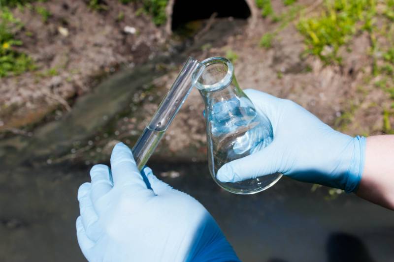 hands holding a beaker outside above wastewater