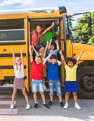 Photo of children celebrating in front of a yellow school bus.