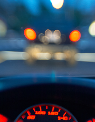 Photo of a speedometer on a car dashboard with lights blurred through the windshield.