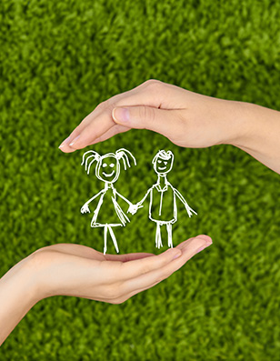 White child's drawing of a boy and girl held between two hands over a grenn grass background.