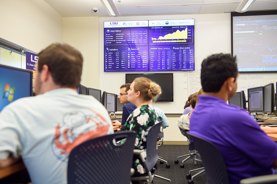 Students working in computer lab with stock market screens in background.