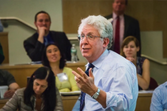 Man with white hair lectures to studnets