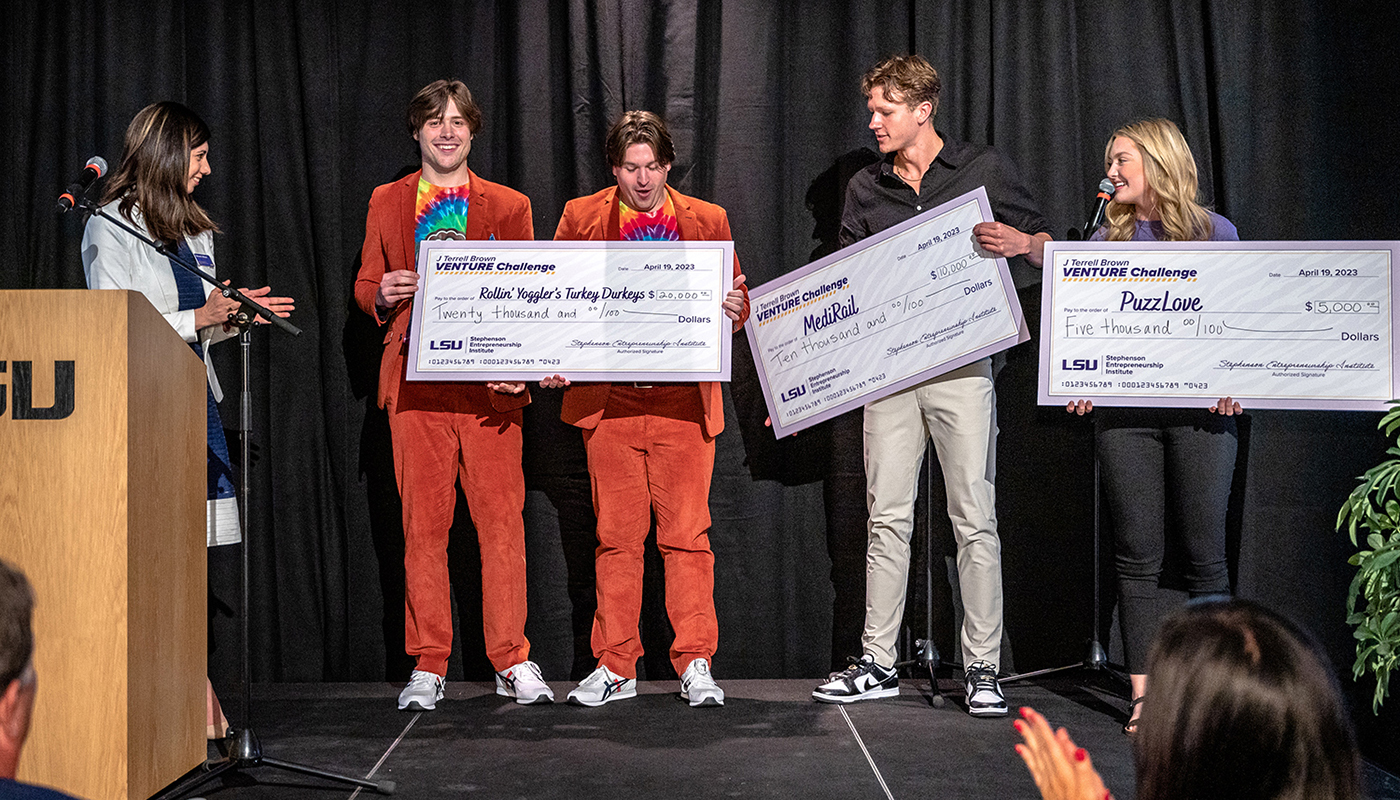 Students hold giant cardboard checks and smile with excitement as prizes are distributed on stage at the 2023 J Terrell Brown Venture Challenge.